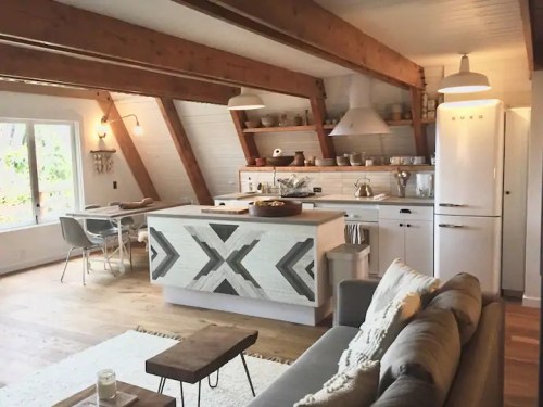 Bright, modern kitchen with wooden beams, white appliances, and a cozy living area featuring a gray sofa and coffee table.