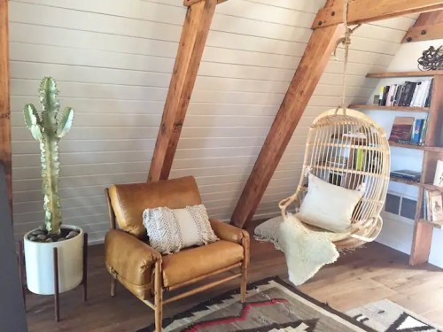 Cozy interior with a leather chair, hanging chair, cactus, and wooden beams in a bright, modern space.