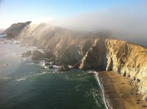 A scenic coastal view featuring cliffs, a sandy beach, and mist rolling over the landscape.