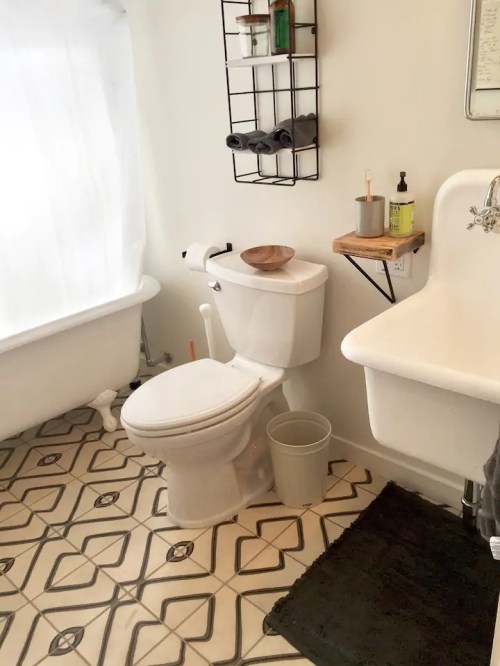 A bright bathroom featuring a toilet, sink, and a vintage bathtub with patterned tiles on the floor.