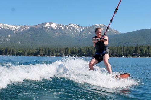 A person water skiing on a lake with mountains in the background, surrounded by trees and clear blue skies.