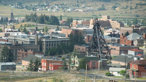 Aerial view of a small town with industrial buildings and mining structures, surrounded by hills and greenery.