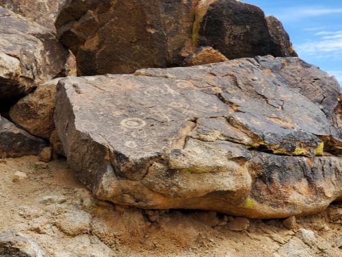 Petroglyphs etched into a large rock surface, surrounded by smaller stones and sandy ground.