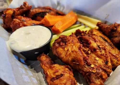 A plate of spicy chicken wings with celery, carrots, and a side of ranch dressing.