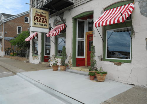 A quaint Italian pizza and ice cream shop with red and white striped awnings and potted plants at the entrance.