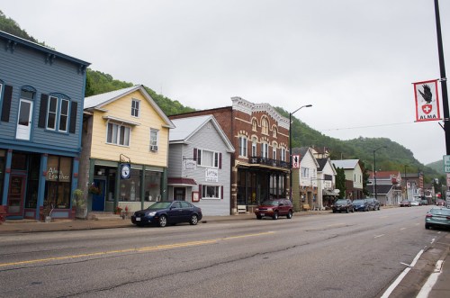 A quaint small-town street lined with colorful shops and buildings, set against a misty green hillside.