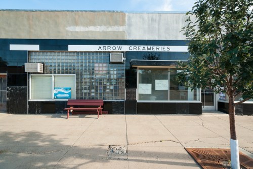 Exterior of Arrow Creameries, featuring a black and white facade, large windows, and a bench in front.
