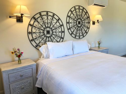 A cozy bedroom featuring a white bed, decorative wall art, and bedside tables with small flower arrangements.