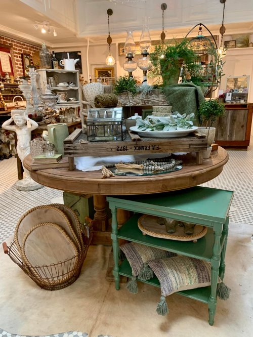 A rustic display table with decorative items, plants, and kitchenware in a charming shop setting.