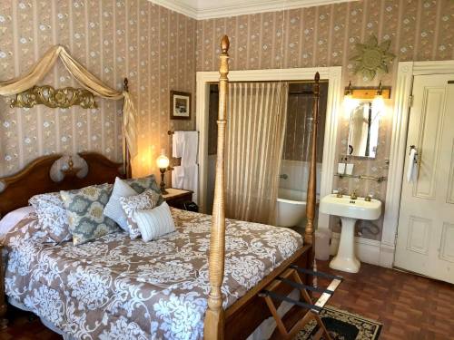 A cozy bedroom with a four-poster bed, patterned wallpaper, and an adjoining bathroom area.