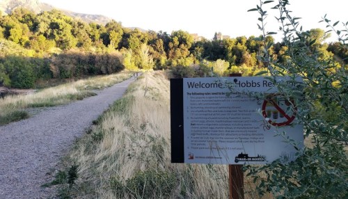 A trail leading into a green area with a sign welcoming visitors to Hobbs Reserve. Trees line the path in the background.