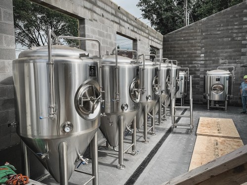 A row of stainless steel fermentation tanks in a partially constructed building.