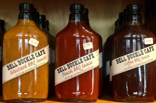 Three bottles of BBQ sauce on a shelf: Mustard BBQ, Peach BBQ, and Coffee BBQ, each with price tags.