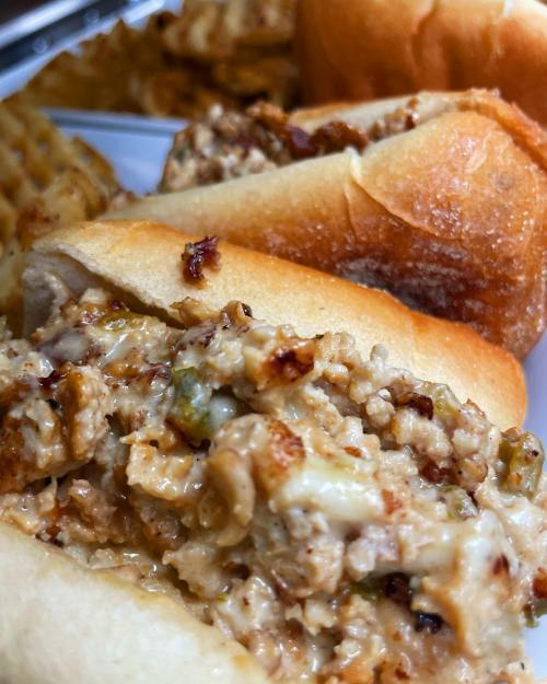 Close-up of a sandwich filled with creamy chicken salad, served with waffle fries in the background.