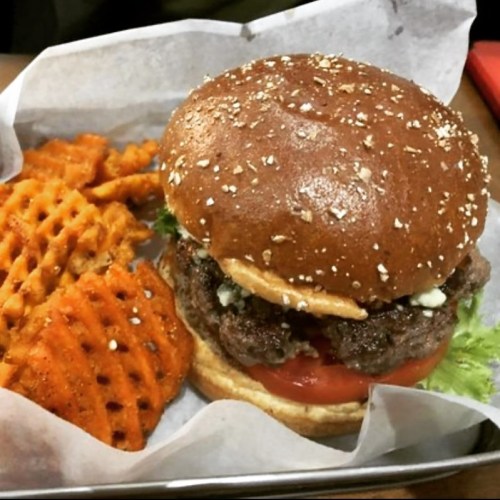 A juicy burger with lettuce, tomato, and blue cheese on an oat-topped bun, served with crispy sweet potato waffle fries.