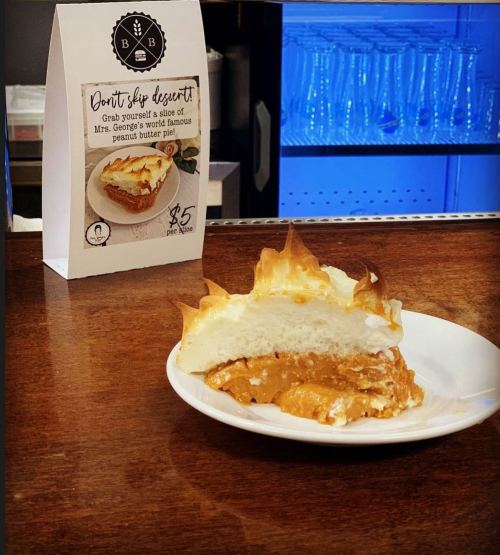A slice of peanut butter pie on a plate, with a sign promoting Mrs. George's famous dessert for $5.
