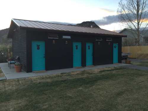 A modern black building with four turquoise doors, set against a scenic backdrop of mountains and trees.