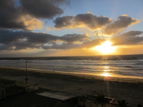 A serene beach scene at sunset, with waves gently lapping the shore and clouds illuminated by the sun.