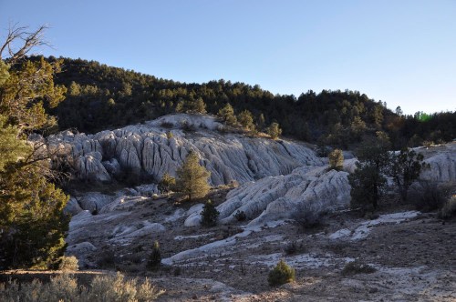 A rocky landscape with layered formations and sparse trees under a clear blue sky.