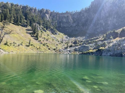 A serene lake surrounded by rocky cliffs and lush greenery under a clear blue sky.