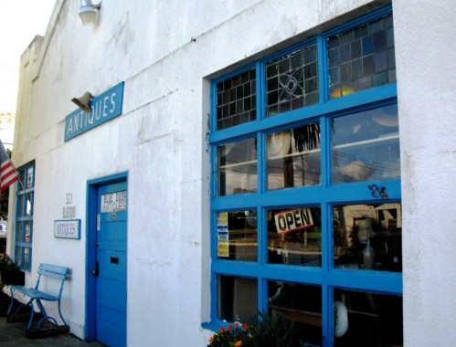 A white building with blue accents, featuring an "Antiques" sign and an "Open" sign in the window.