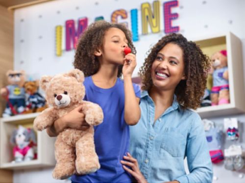 A smiling mother and daughter hold a teddy bear, with the word "IMAGINE" displayed in the background.