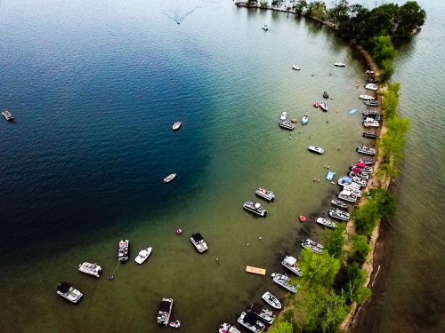 Aerial view of a lake with numerous boats anchored along a shoreline surrounded by trees.