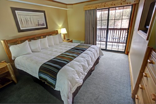 Cozy hotel room with a king-sized bed, wooden accents, and a balcony overlooking a natural view.