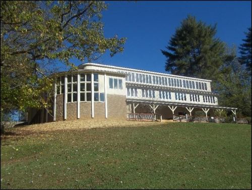 A modern building with large windows, set on a grassy hill under a clear blue sky, surrounded by trees.