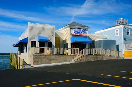 Exterior of Bubba's Seafood Restaurant with blue awnings, located by the water under a clear blue sky.