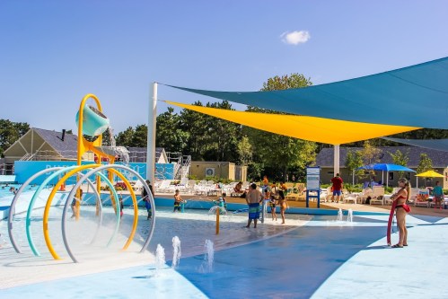 A vibrant water park scene with colorful slides, splash features, and people enjoying the sunny day under shade sails.