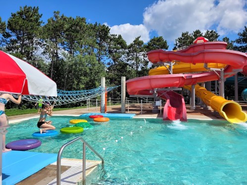 A colorful water park scene featuring a water slide, floating rings, and children playing in a pool under a blue sky.