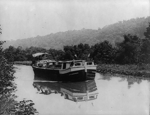 A vintage boat on a calm river, surrounded by lush greenery and hills in the background.