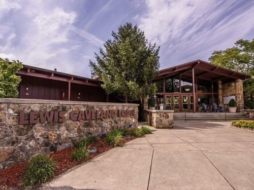 Exterior view of Lewis Cavern Lodge, featuring stone walls, greenery, and a modern architectural design under a blue sky.