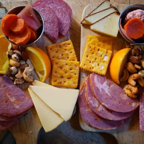 A wooden platter with assorted meats, cheeses, nuts, fruits, and pickled vegetables arranged beautifully.