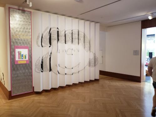 A gallery wall with a playful monkey design and text, featuring a wooden floor and a visitor in the background.