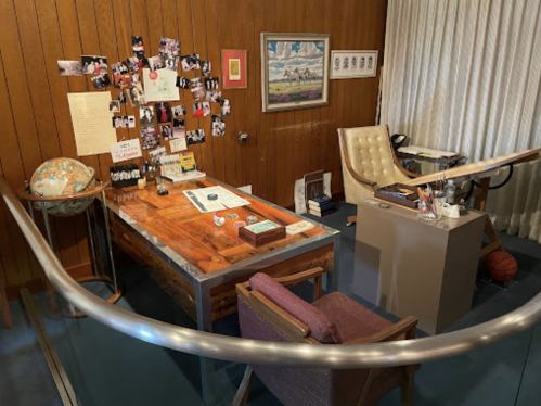 A cozy office space featuring a wooden desk, chair, globe, and wall photos, with a basketball on the floor.
