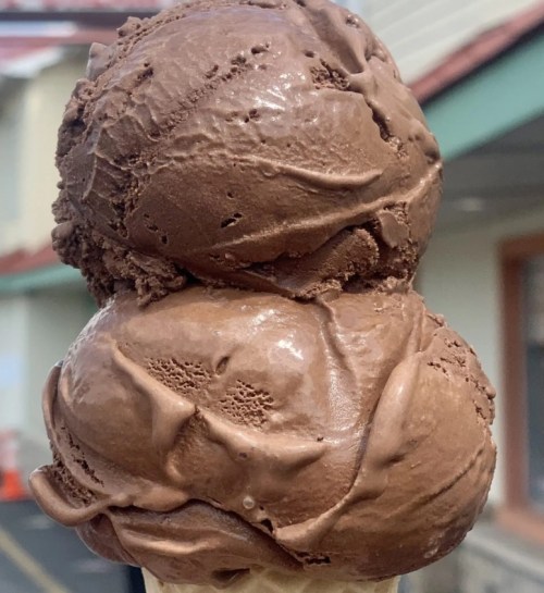 A close-up of a double scoop of rich chocolate ice cream on a cone, with a smooth, creamy texture.