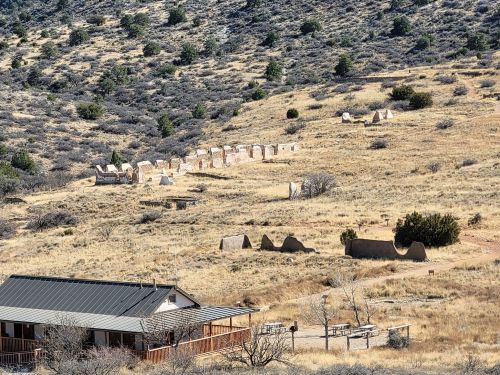 A landscape view of a dry, hilly area with scattered ruins and a small building in the foreground.