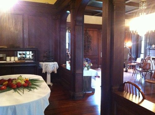 A cozy, vintage dining room with wooden paneling, tables set with fruit, and elegant lighting.