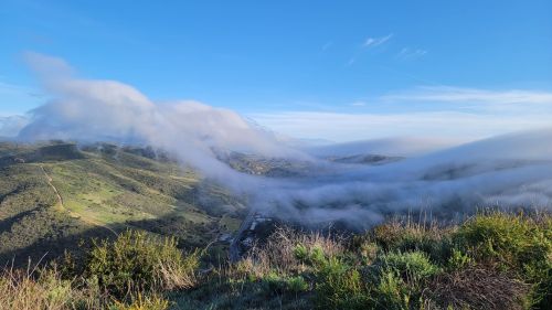 A scenic view of rolling hills and valleys shrouded in mist under a clear blue sky.