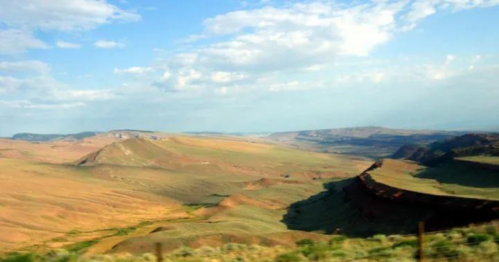 A vast landscape of rolling hills and valleys under a blue sky with scattered clouds.