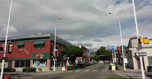 A street view featuring shops, traffic lights, and cloudy skies in a small town.