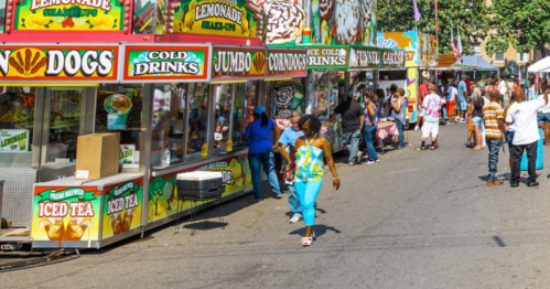 A vibrant street fair scene with food stalls, colorful signage, and people enjoying the festivities.