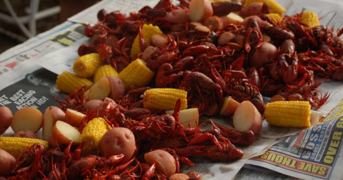 A spread of boiled crawfish, potatoes, corn, and sausage on newspaper, ready to be served.