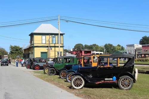 A row of vintage cars parked along a street near a yellow building on a clear day.