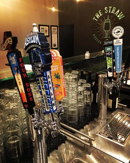 A bar counter with various beer taps, glasses, and a sign reading "The Straw - Modern Elysian."