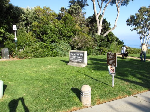 Sign for Crescent Bay Point Park surrounded by greenery, with a view of the ocean in the background.