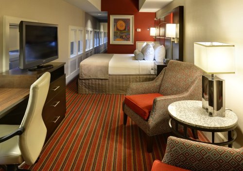 Cozy hotel room featuring a bed, desk, TV, and seating area with colorful decor and striped carpet.