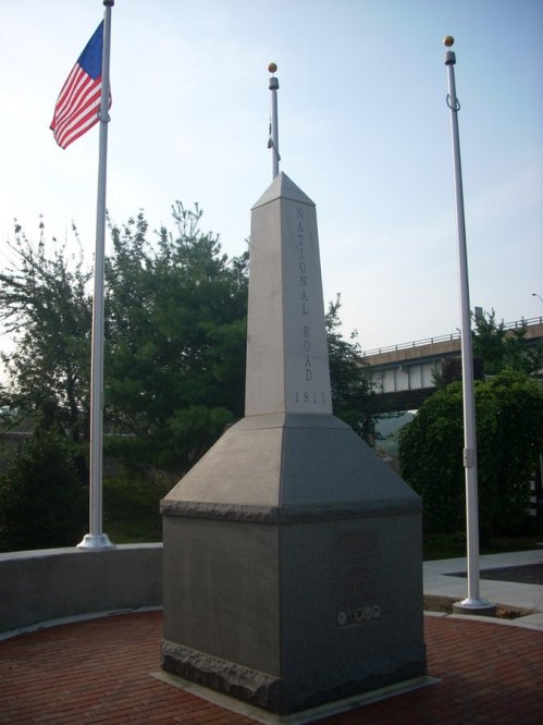 Monument marking the National Road, 1811, surrounded by flags and greenery.